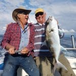 Two men laughing and one is holding a large fish